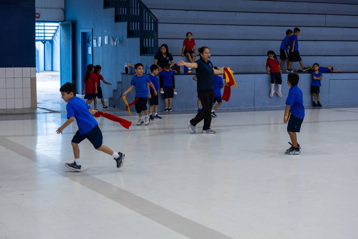 Students in uniform playing a flag game during PE class in the school gymnasium