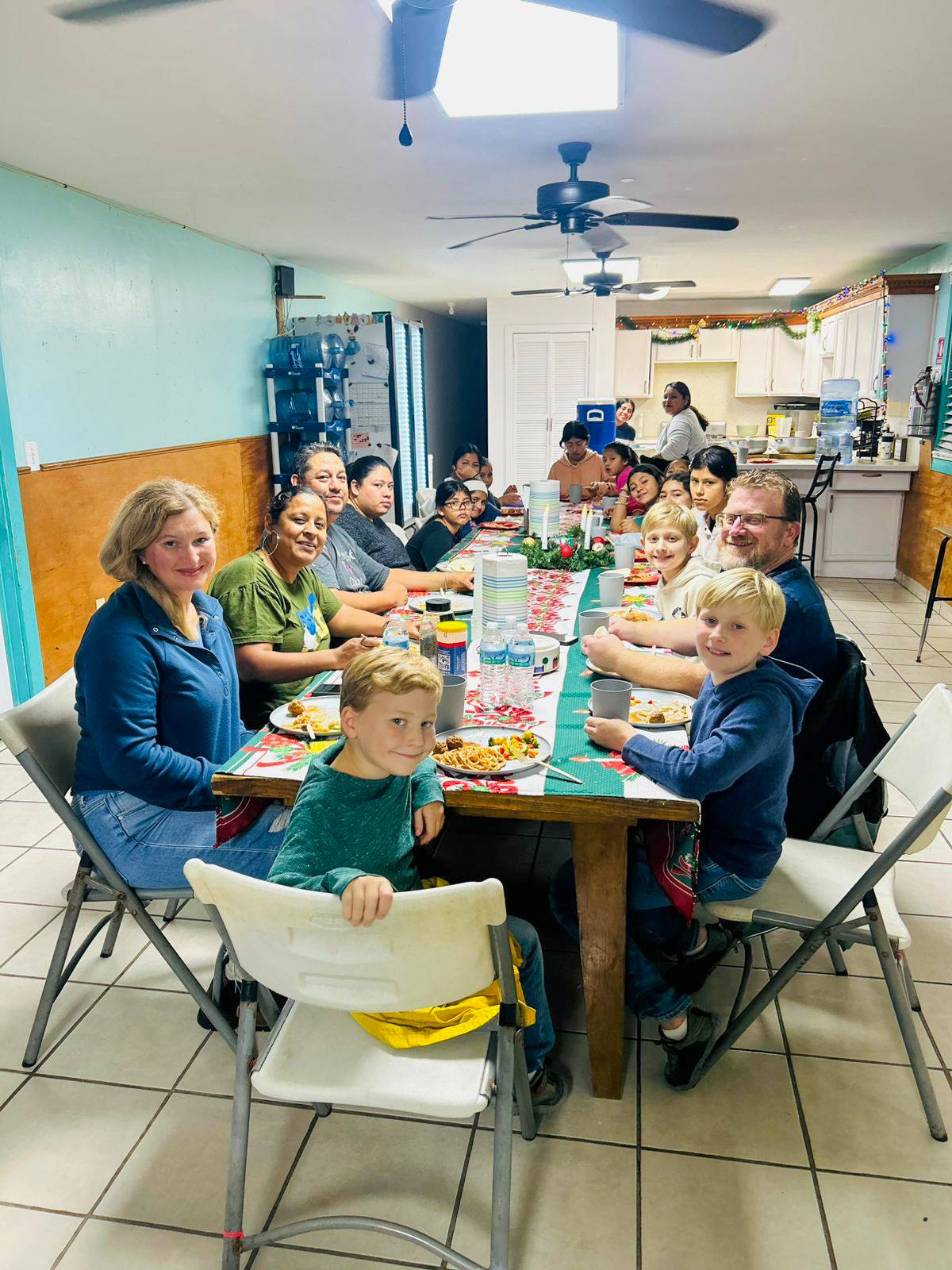 A visiting family sharing a meal at a long table with children and staff at Casa Hogar Rio Bravo