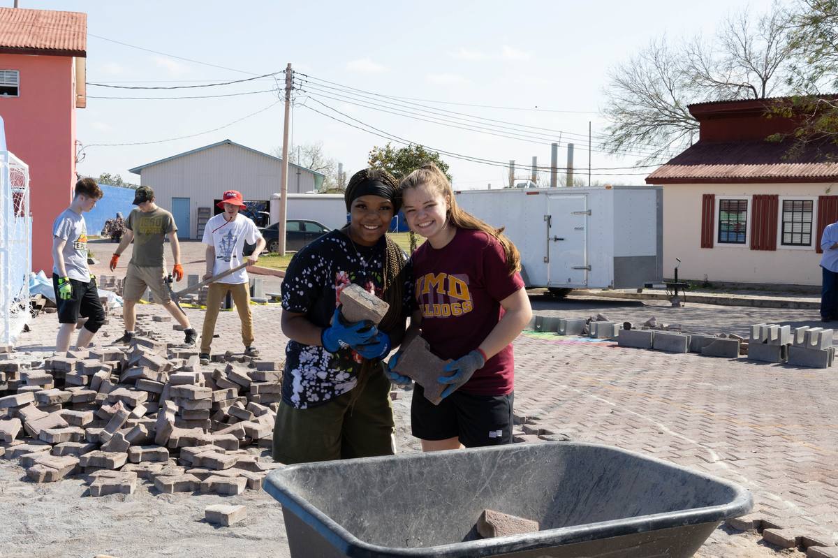 Two student volunteers carrying pavers during a campus improvement project